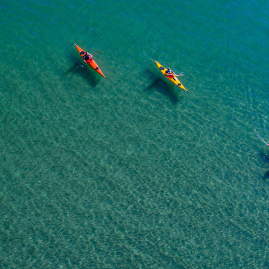 Three people kayaking through light blue waters 